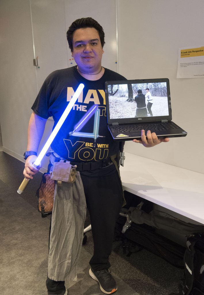 Student presenting their work on a laptop and a lightsaber at IDM showcase 2018